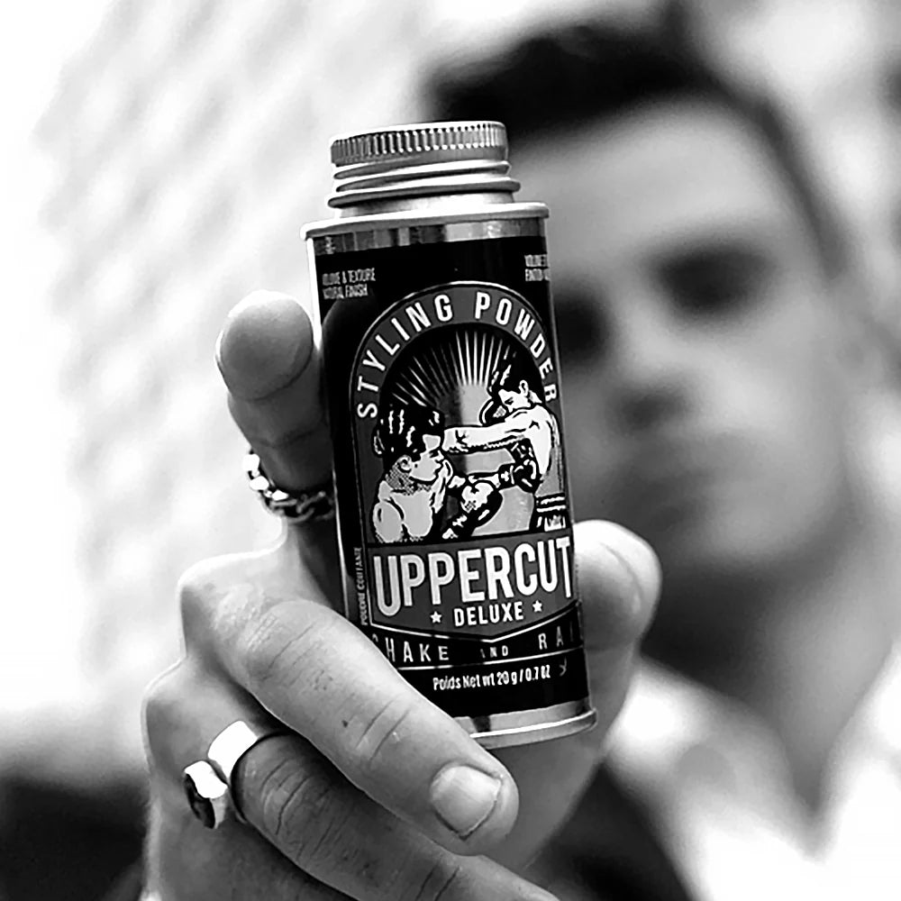 Hand holding a can of Uppercut Deluxe Styling Powder with a blurred background. Close-up of Uppercut Deluxe Styling Powder 20g – buildable hold hair powder for men.